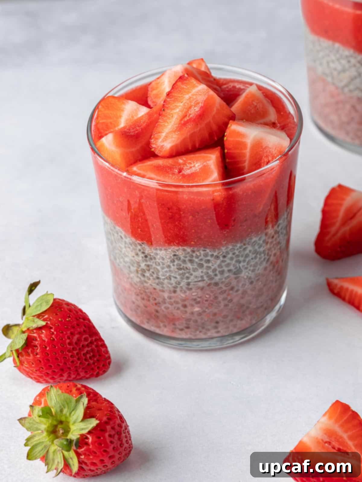 Creamy Strawberry Chia Pudding 6 A close-up shot of a glass of layered strawberry chia pudding, topped with fresh strawberries and a mint sprig, ready to be served.