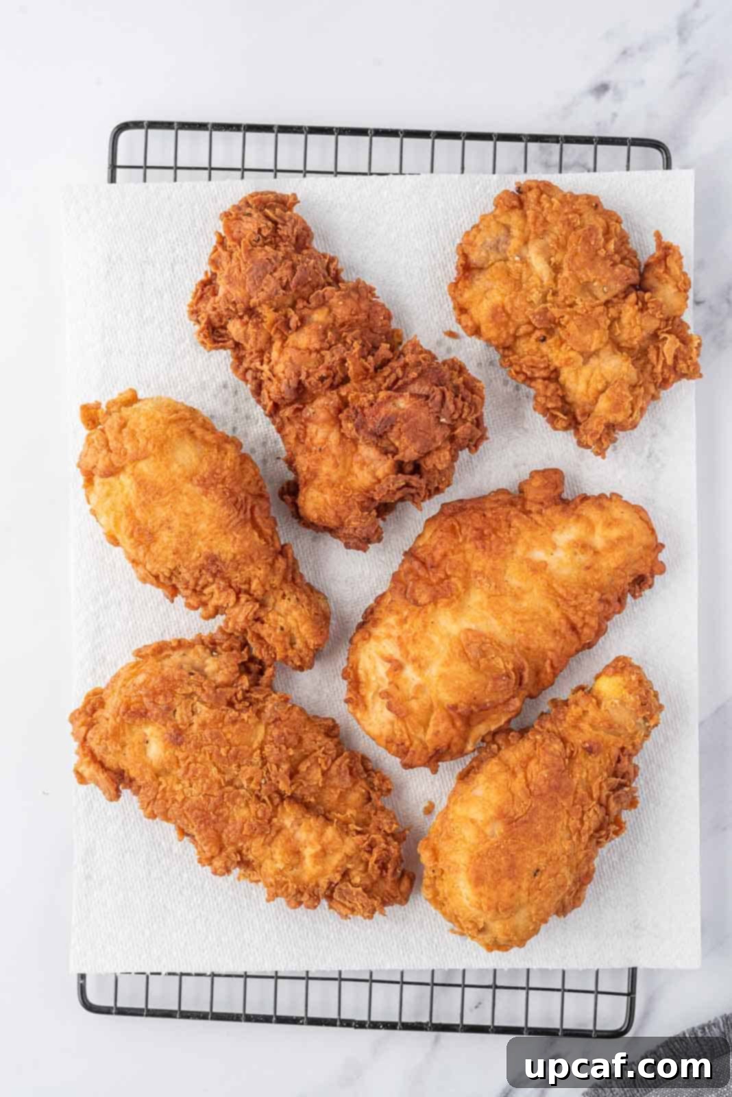 Crispy Fried Chicken Perfection 7 Extra crispy fried chicken draining on paper towels on a wire rack.