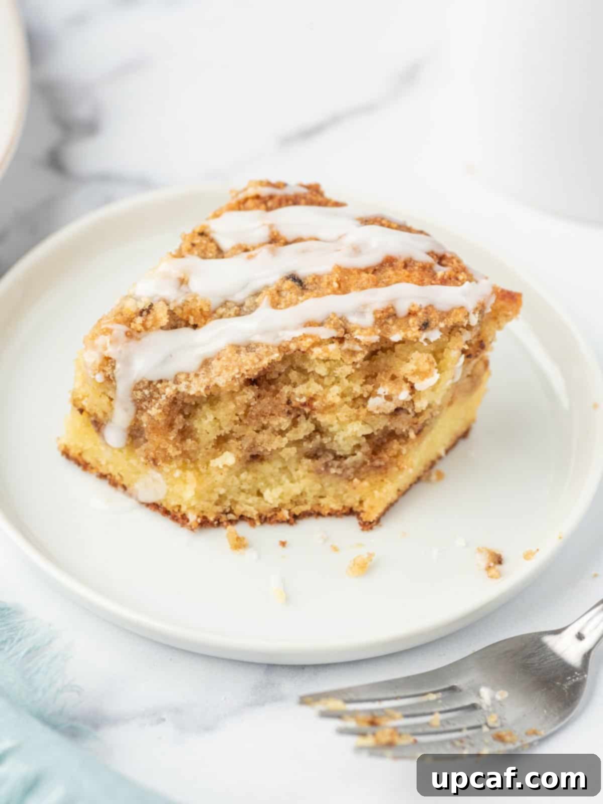A delectable piece of low carb coffee cake with a bite missing, resting on a white plate with a few crumbs. A fork with crumbs sits to the side, highlighting the irresistible nature of the almond flour coffee cake.