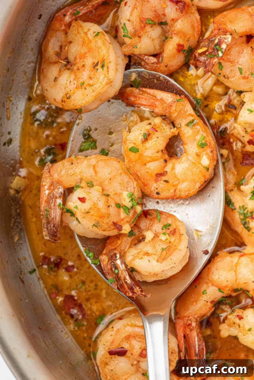 A serving spoon lifting a piece of perfectly cooked lemon garlic butter shrimp from the skillet.