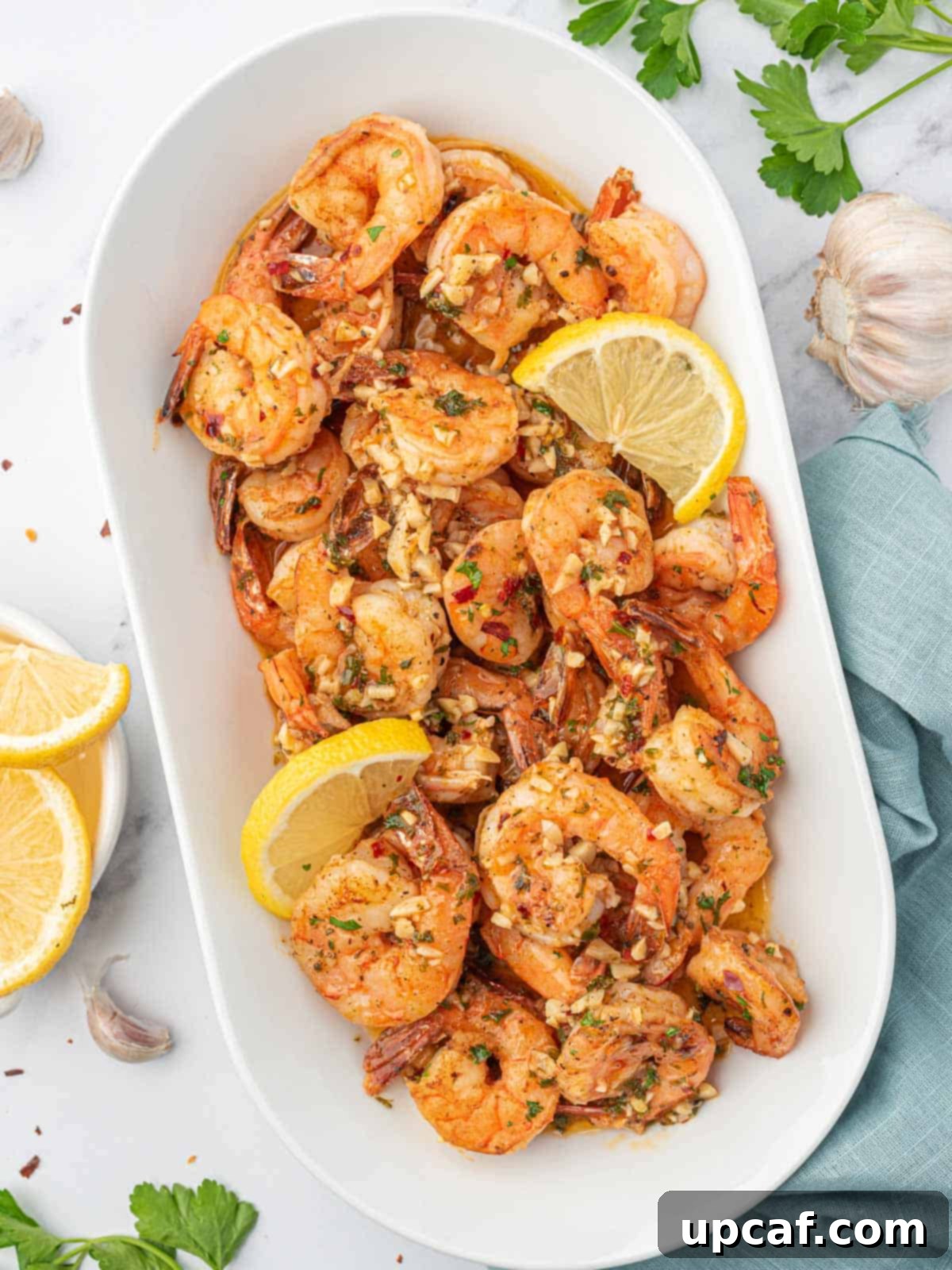 A large serving tray filled with glistening garlic and lemon shrimp, garnished with fresh herbs and lemon wedges.