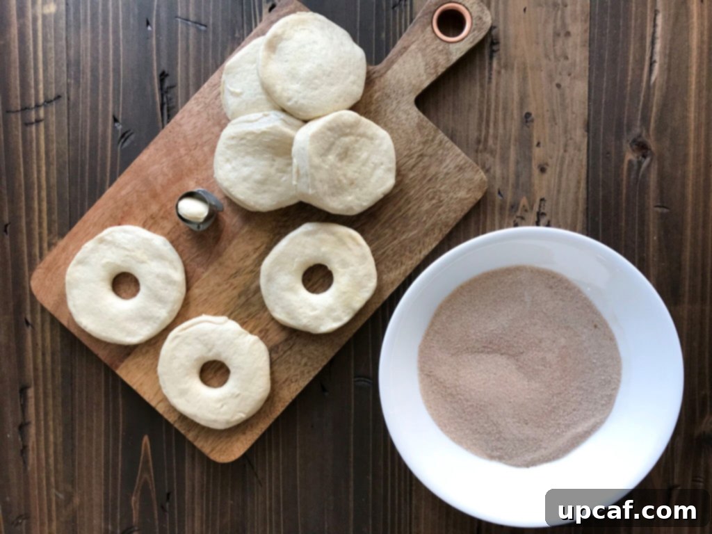 Pillsbury biscuit dough on a wooden board with holes cut out, ready for frying.
