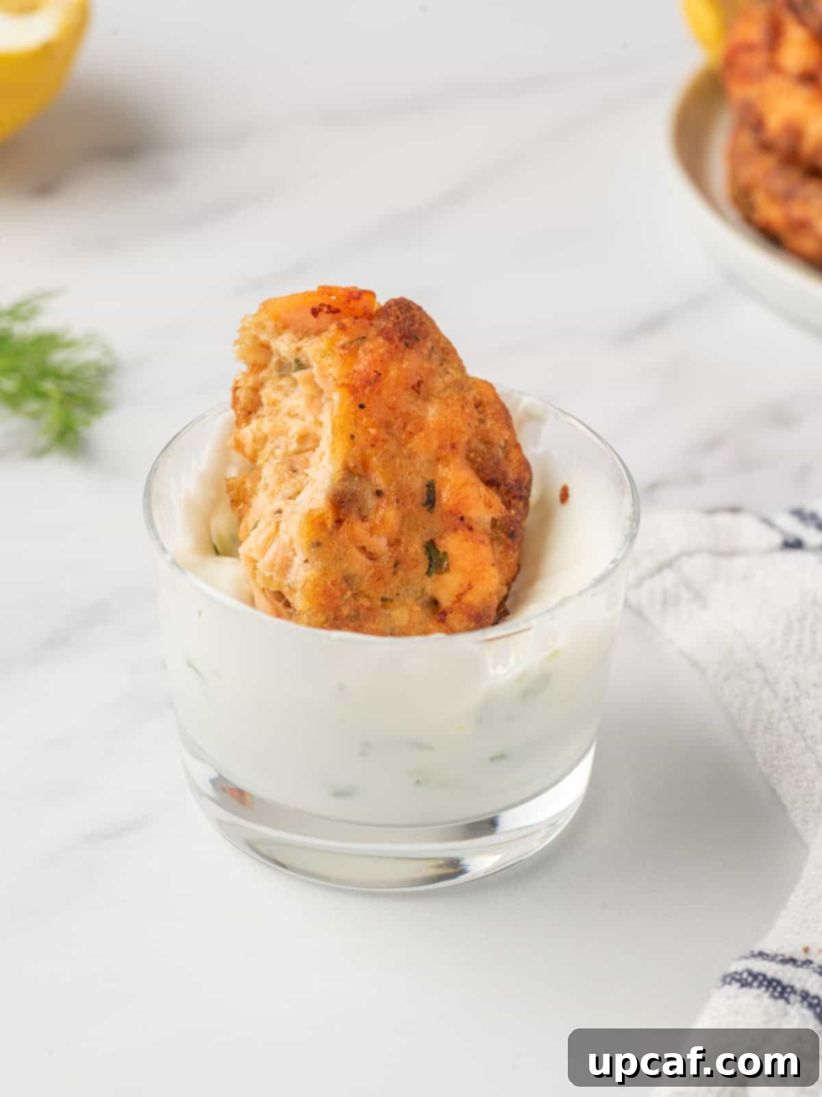 A bite of Salmon patties with bread crumbs being dunked in tzatziki sauce.