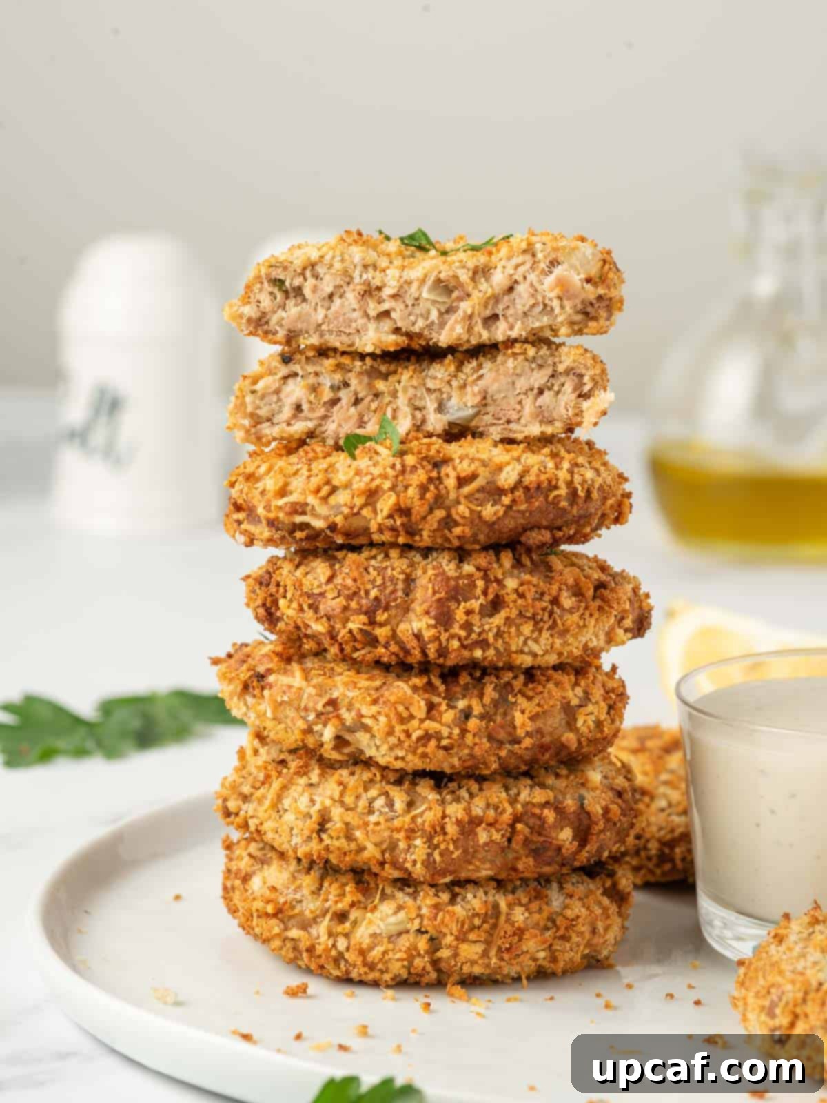 A close-up of a stack of golden brown crispy tuna cakes on a white plate, ready to be served.