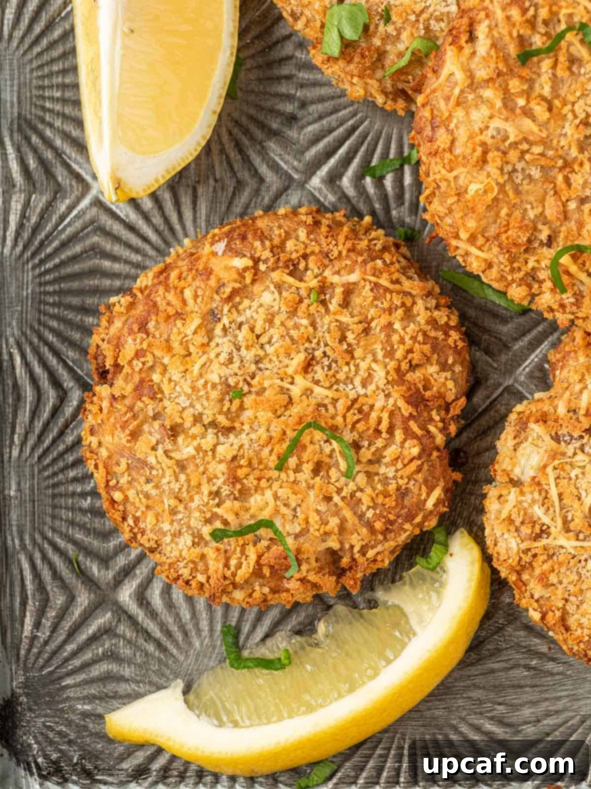 Close-up of golden brown canned tuna fish cakes, garnished with fresh parsley and lemon wedges, ready to be enjoyed.