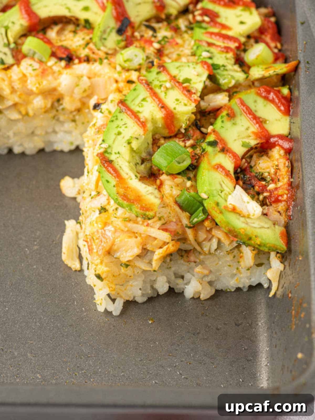 Imitation crab sushi bake garnished with avocado, green onions, and sriracha in a casserole dish.