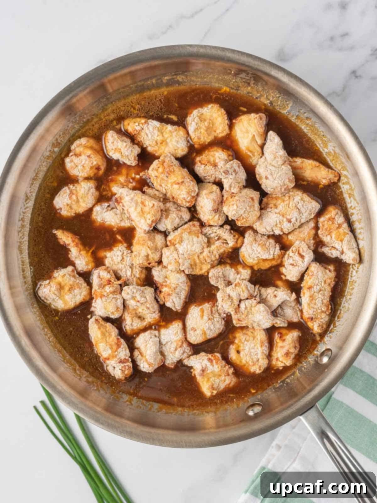 Crispy Air-Fried Orange Chicken 7 Crispy air-fried chicken pieces being tossed vigorously in a skillet with the freshly made sticky orange sauce, ensuring every piece is evenly coated.