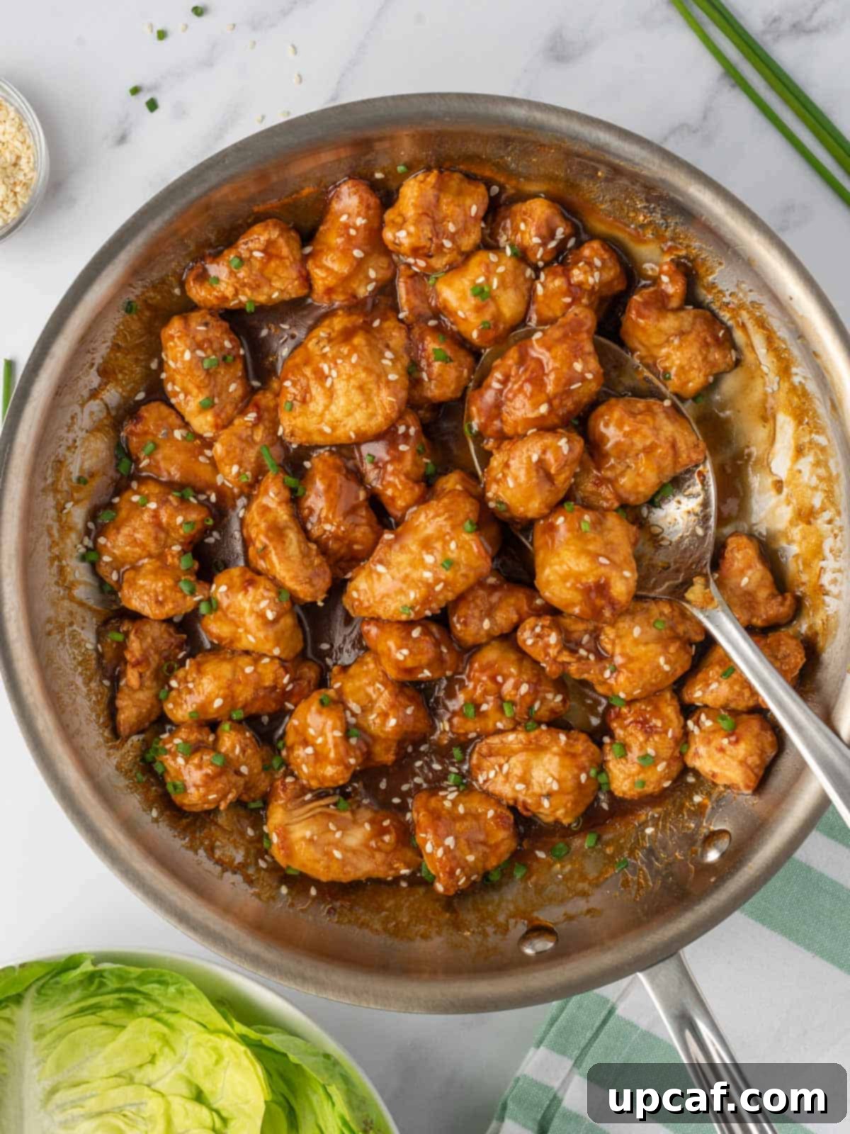 Crispy Air-Fried Orange Chicken 8 A close-up of a skillet filled with glistening, sauced crispy air fryer orange chicken, ready to be served, accompanied by a serving spoon.