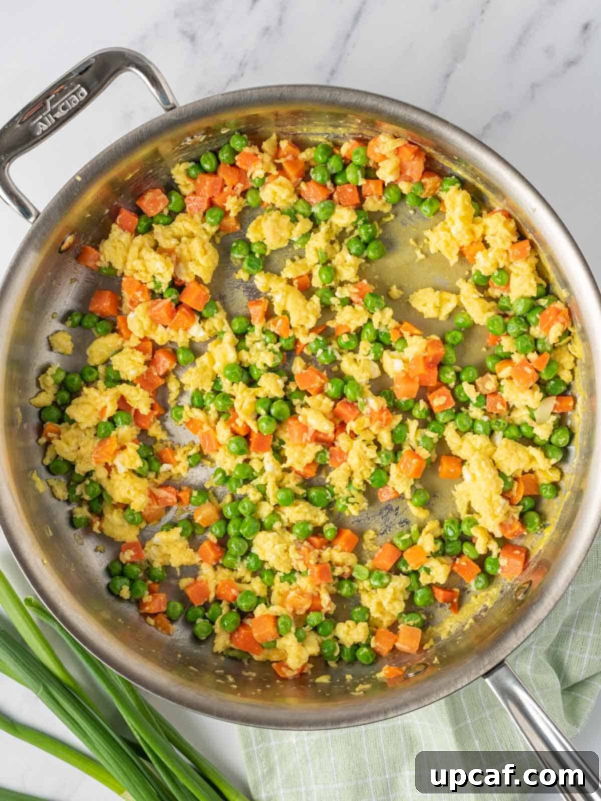 The process of cooking eggs and mixed vegetables in a skillet for Chinese vegetarian fried rice.