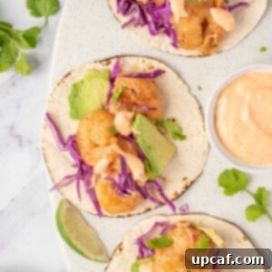 Three bang bang shrimp tacos with dynamite sauce sit on a serving platter.
