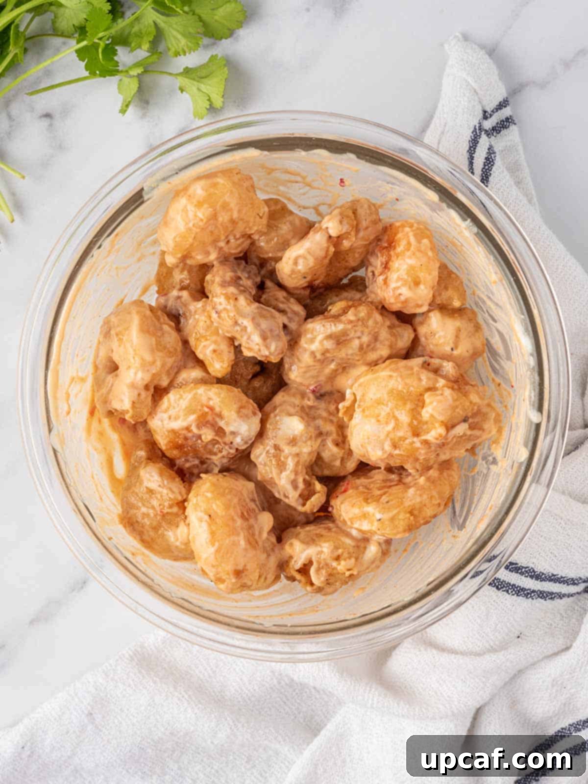 Close-up of fried shrimp being coated in a creamy, orange spicy dynamite shrimp sauce.