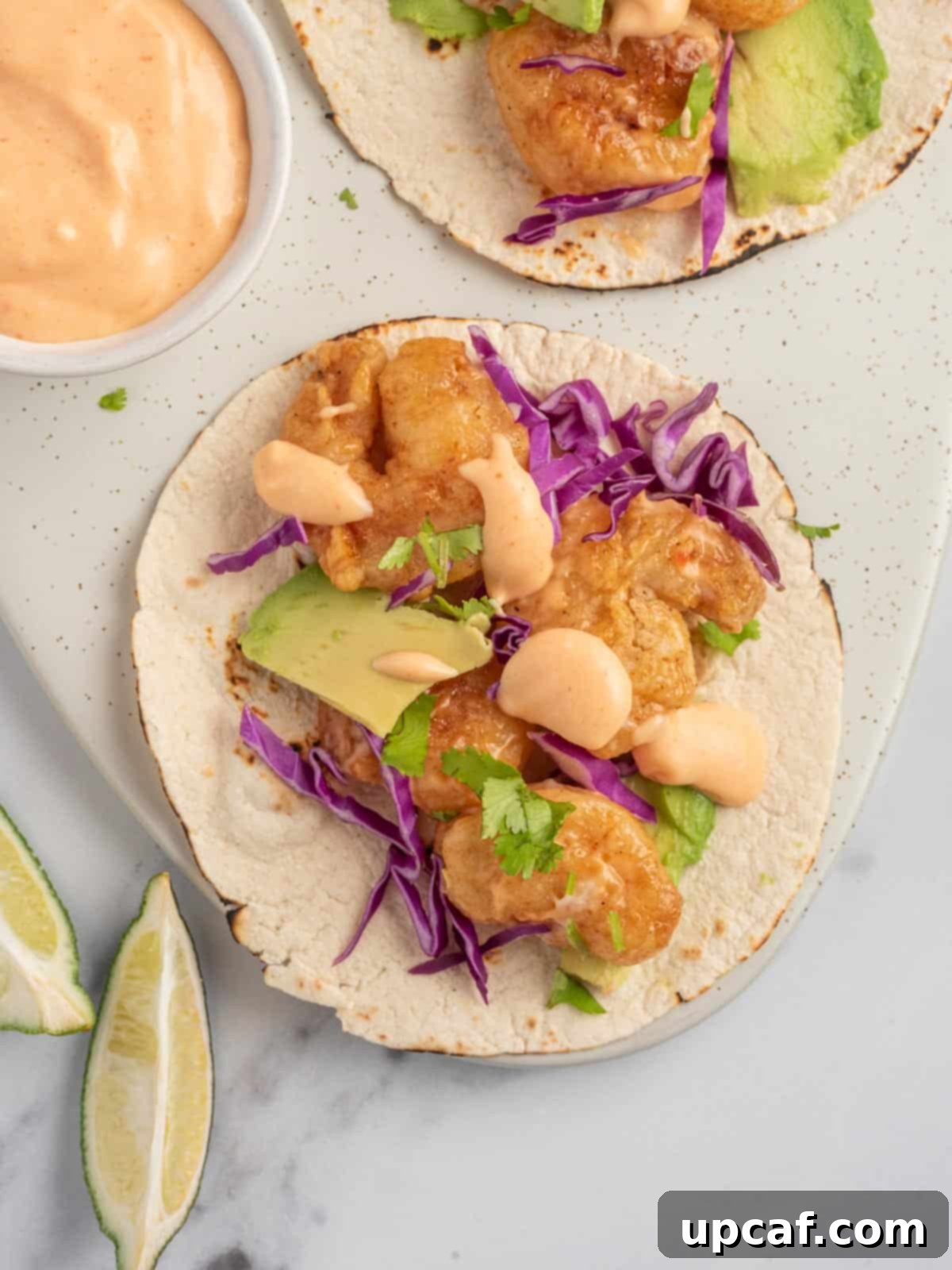 An assembled spicy shrimp taco with bang bang sauce, cilantro, and lime on a serving platter.