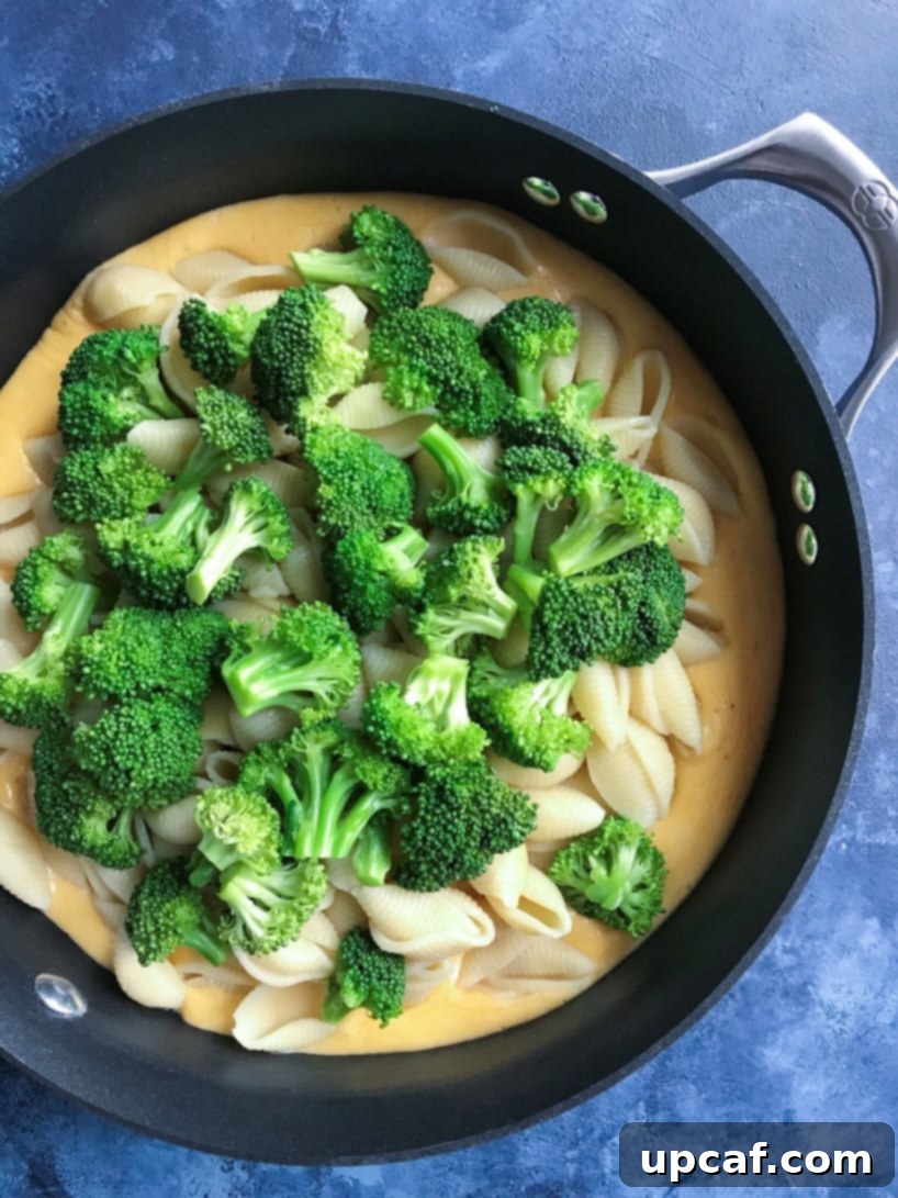 Broccoli florets being added to mac and cheese in a skillet.