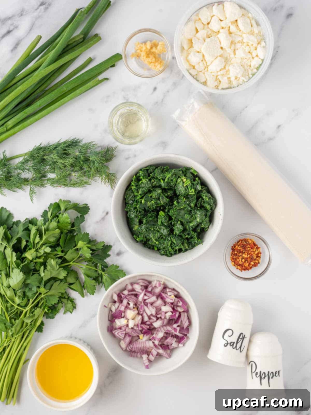 Quick & Easy Spanakopita Bites 3 A selection of fresh ingredients laid out, including spinach, feta cheese, herbs, onion, garlic, olive oil, and phyllo dough sheets, ready for making easy spanakopita.