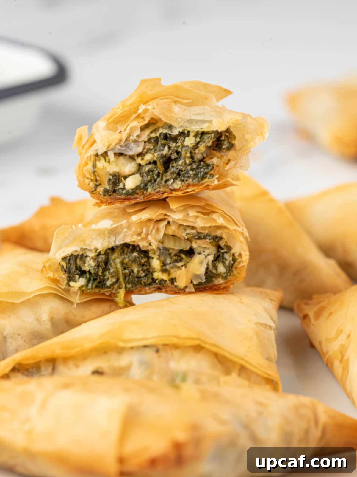 Quick & Easy Spanakopita Bites 9 A close-up shot of a homemade Greek spinach pie triangle, cut in half to reveal the rich spinach and feta filling, stacked on a platter.