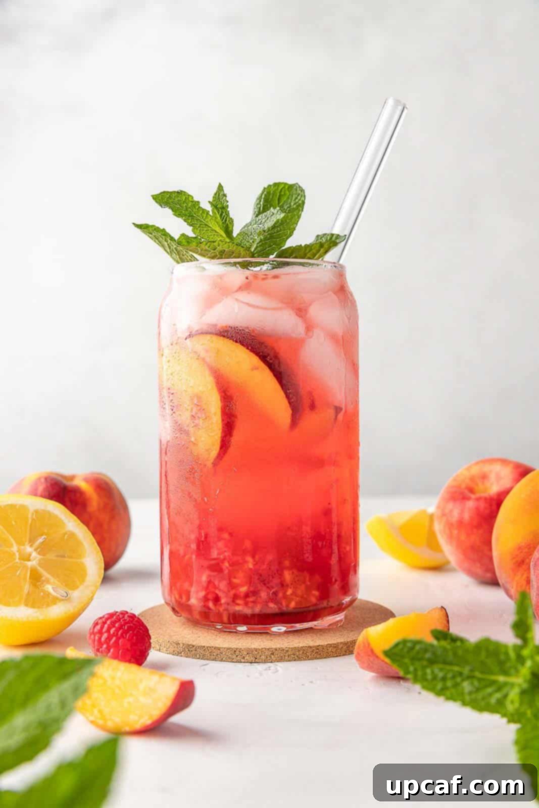 Raspberry Peach Sunburst Quencher 2 A vibrant glass of Raspberry Peach Lemonade Cooler with fresh fruit and a glass straw, perfect for summer.