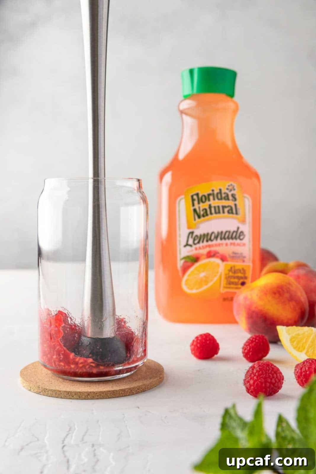 Raspberry Peach Sunburst Quencher 4 Mashing fresh raspberries in a glass to release their vibrant juices and enhance the lemonade flavor.
