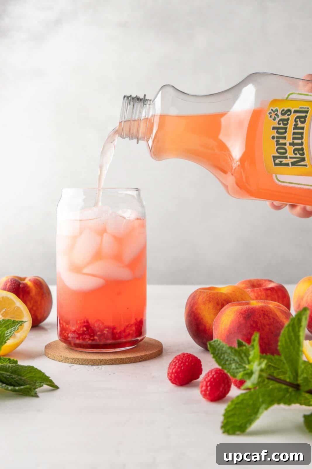 Raspberry Peach Sunburst Quencher 6 Pouring Florida's Natural Raspberry Peach Lemonade into a glass with ice and muddled raspberries.