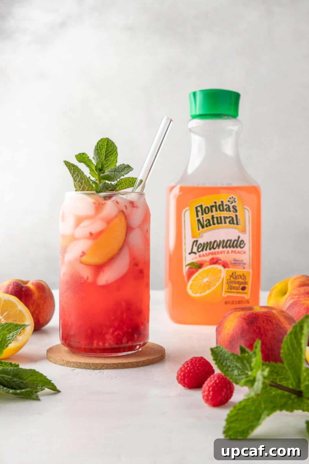 Raspberry Peach Sunburst Quencher 7 A beautifully garnished Raspberry Peach Lemonade Cooler, ready to be enjoyed, with a bottle of Florida's Natural lemonade in the background.