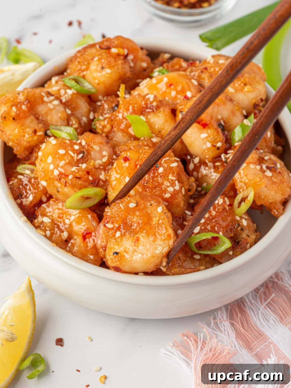 Blazing Burst Shrimp 9 Spicy fried shrimp with firecracker shrimp sauce in a bowl, with a piece being picked up by chopsticks, showcasing the crispy texture.