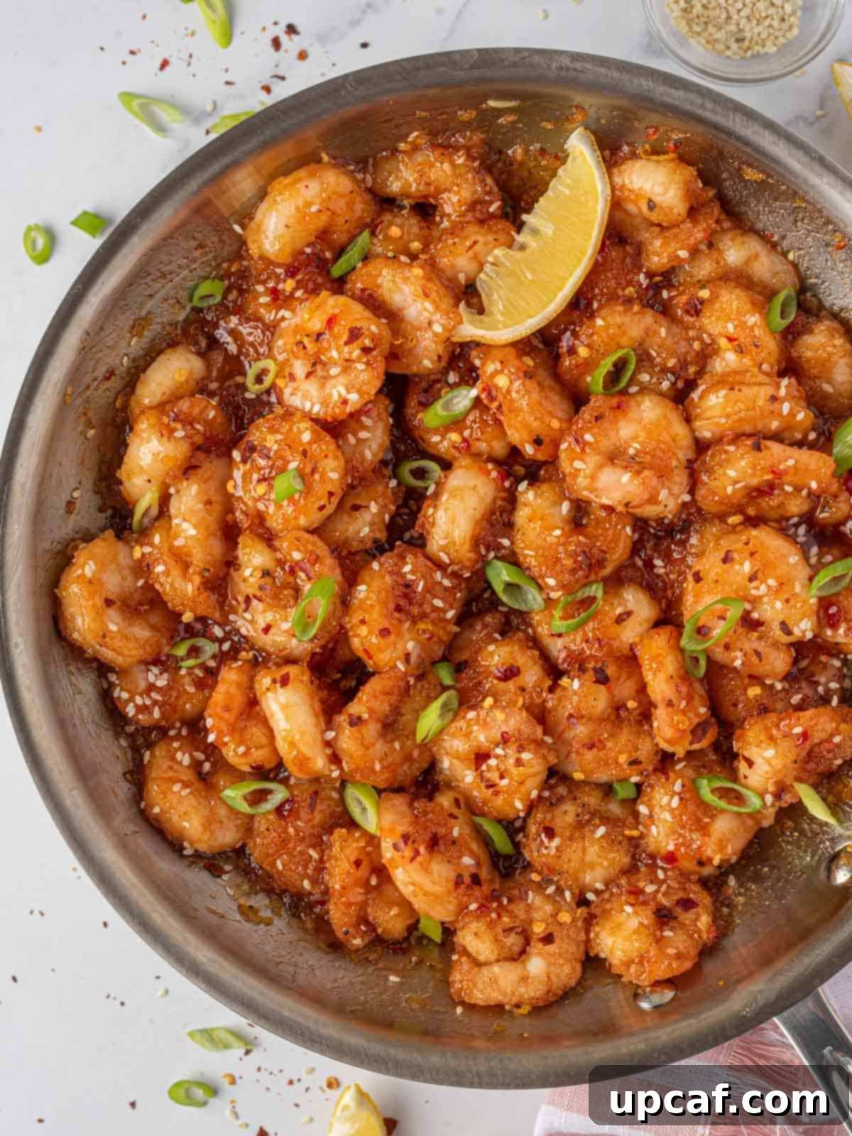 Blazing Burst Shrimp 10 Garnished firecracker shrimp presented in a skillet with a lemon wedge, ready for serving.