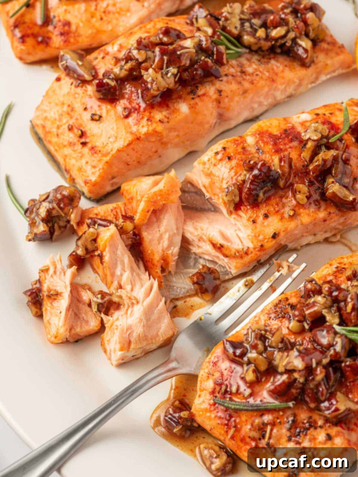 Caramelized Maple Pecan Salmon 7 A close-up of a flaky piece of salmon with maple syrup and pecans on a plate, ready to be eaten with a fork.