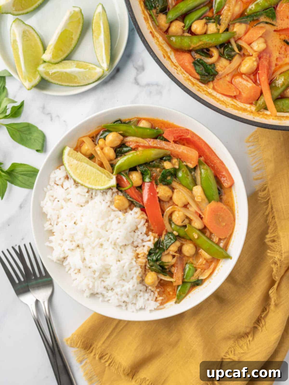 Vibrant Red Thai Plant-Based Curry 2 A bowl of rice with vibrant red Thai vegan curry, garnished with fresh herbs, with a pot of steaming curry in the background, highlighting its creamy and comforting appeal.