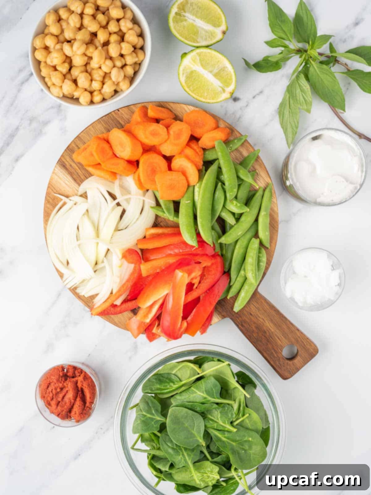 Vibrant Red Thai Plant-Based Curry 3 A carefully arranged collection of fresh ingredients laid out on a table, including coconut oil, minced garlic, grated ginger, sliced yellow onion, vibrant red bell pepper, crisp carrots, hearty chickpeas, tender snow peas, leafy spinach, a jar of red curry paste, canned coconut milk, salt, fresh limes, and aromatic Thai basil, all meticulously prepared and ready for making an exquisite red Thai vegan curry.