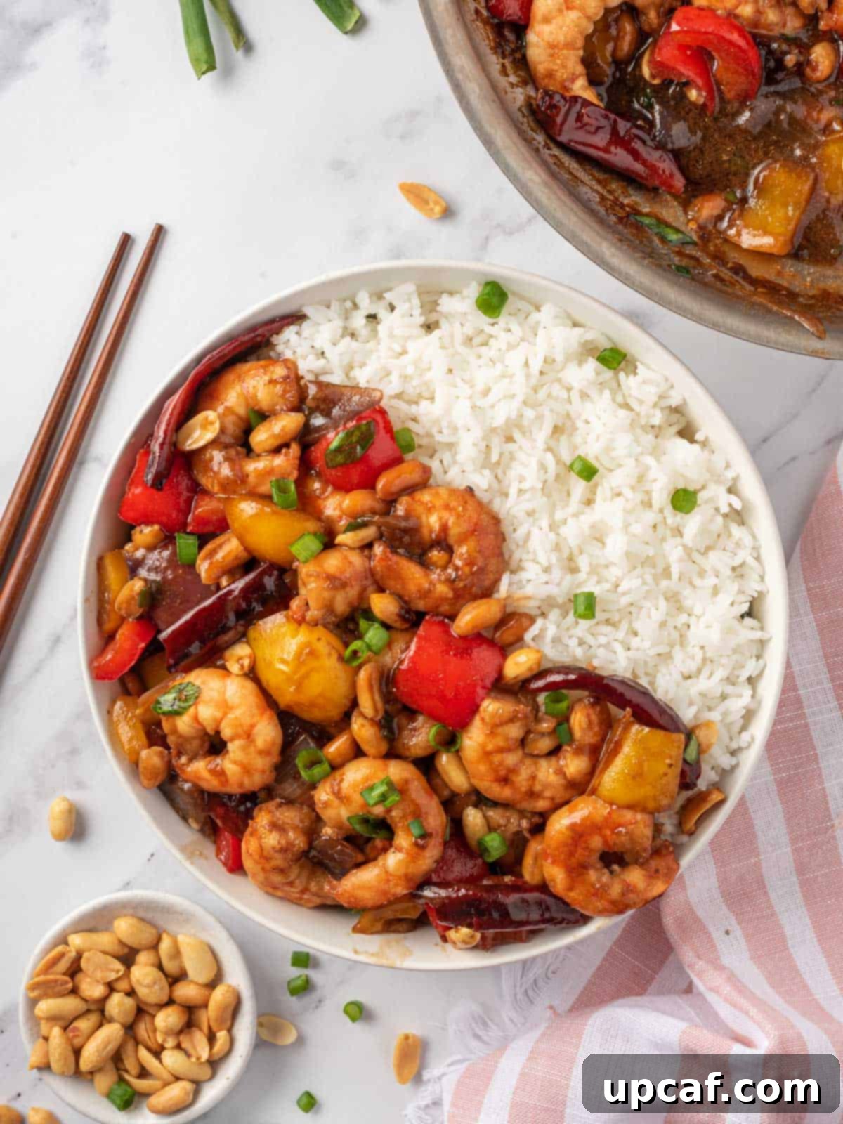 Kung Pao Shrimp recipe in a bowl with rice and chopsticks on the rice, highlighting the vibrant colors and appealing texture of the dish.