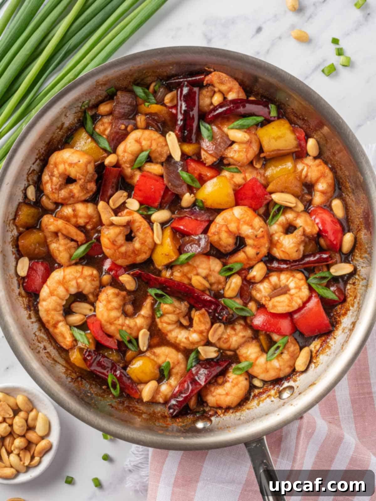 The finished Kung Pao Shrimp dish simmering in a skillet, garnished with green onions and ready to be served.