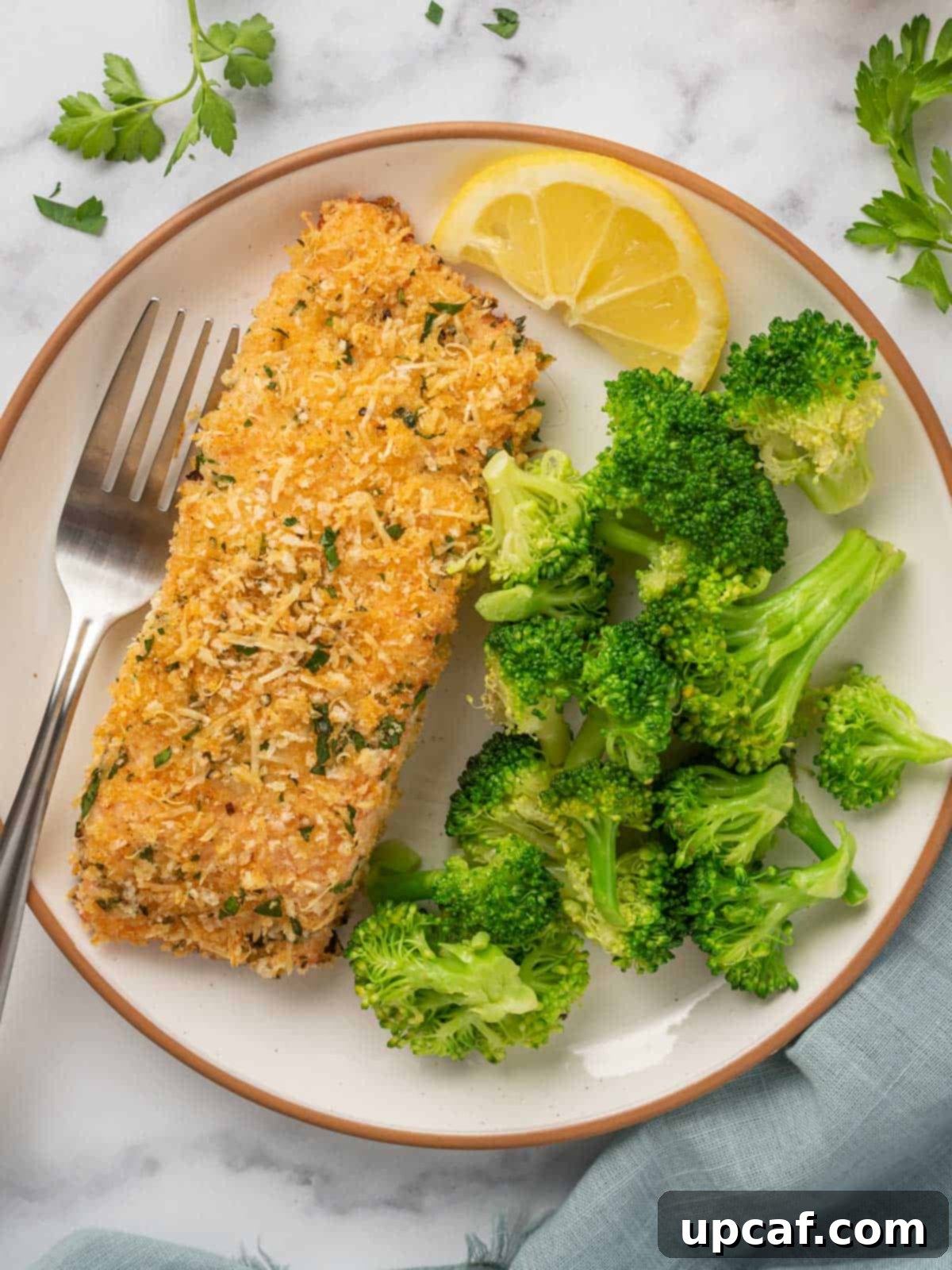 Crispy baked salmon on a plate with a fork and a pile of steamed broccoli.