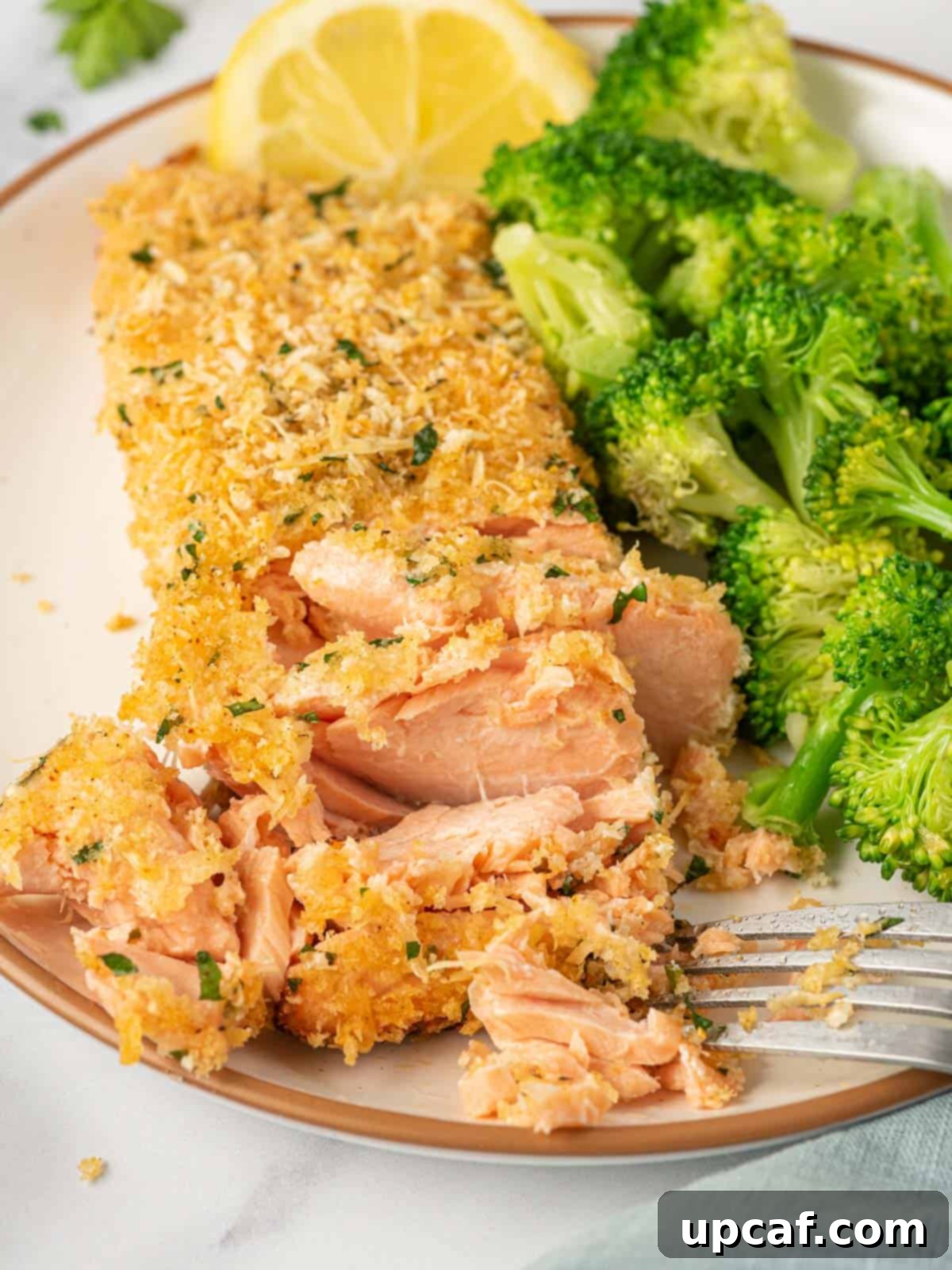 A fork flakes off parmesan crusted salmon recipe.