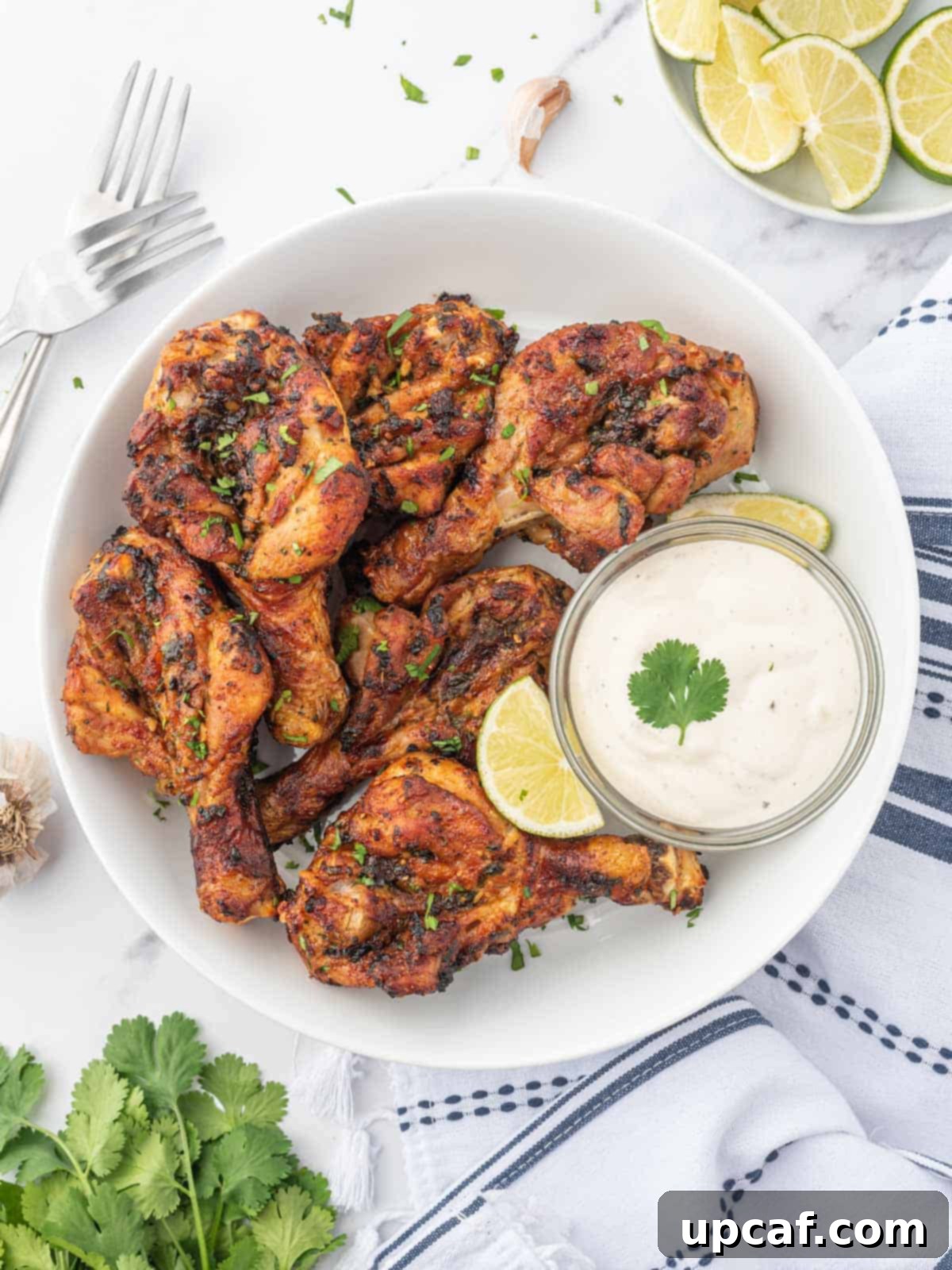 Air-fried butterfly drumsticks marinated in cilantro lime sauce, served with a garnish of fresh cilantro and lime wedges on a white plate. The chicken is golden brown and crispy.