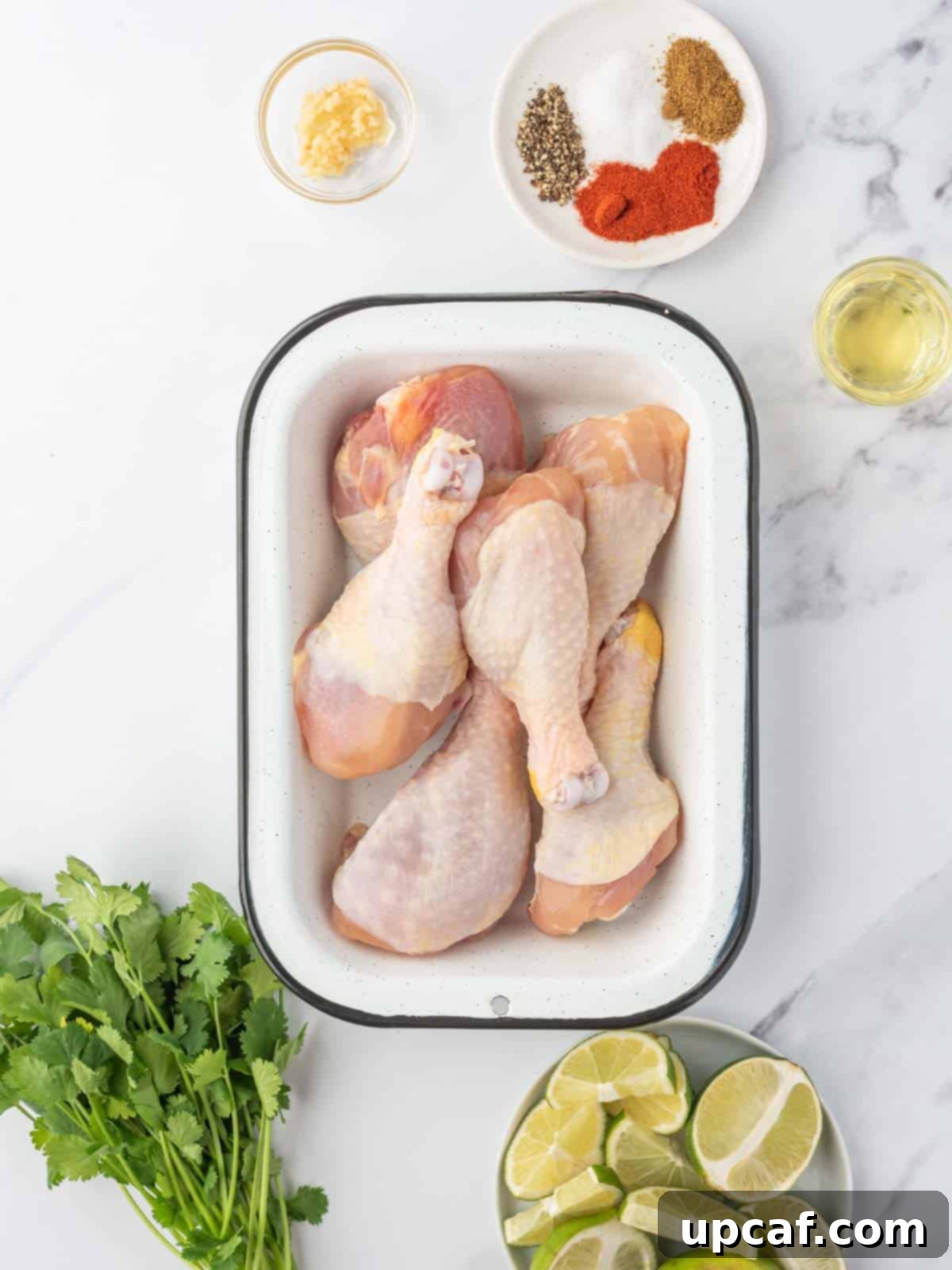 A top-down view of all the fresh ingredients laid out for making butterfly drumsticks, including chicken drumsticks, fresh limes, olive oil, cilantro, garlic, and a selection of spices.