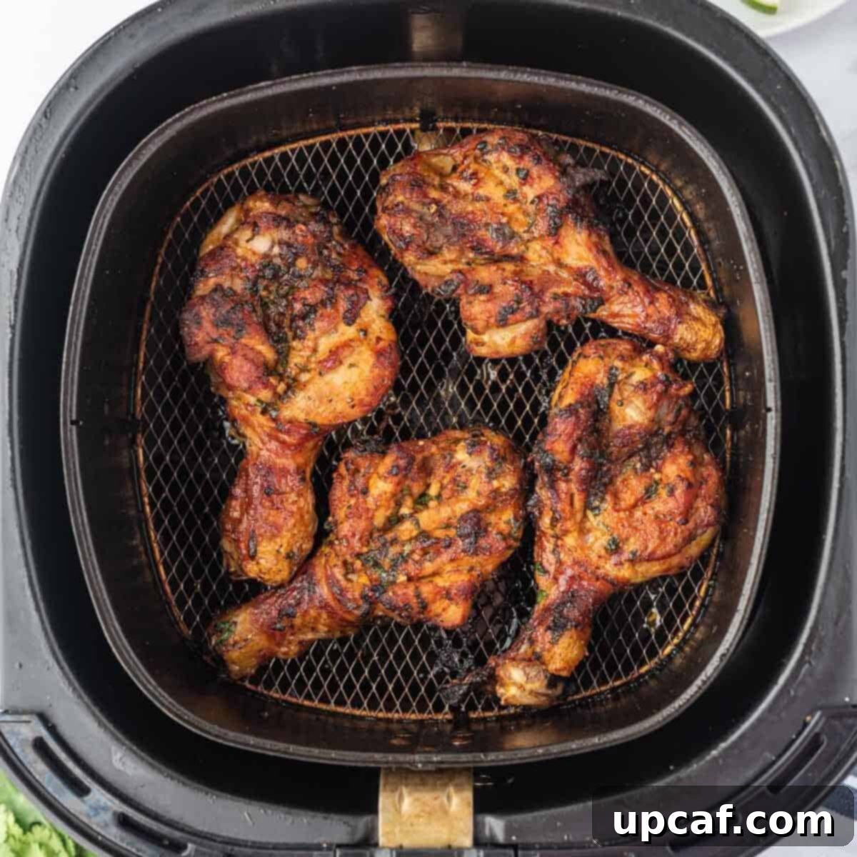 Butterflied chicken drumsticks arranged in a single layer inside an air fryer basket, cooking to a golden crisp.