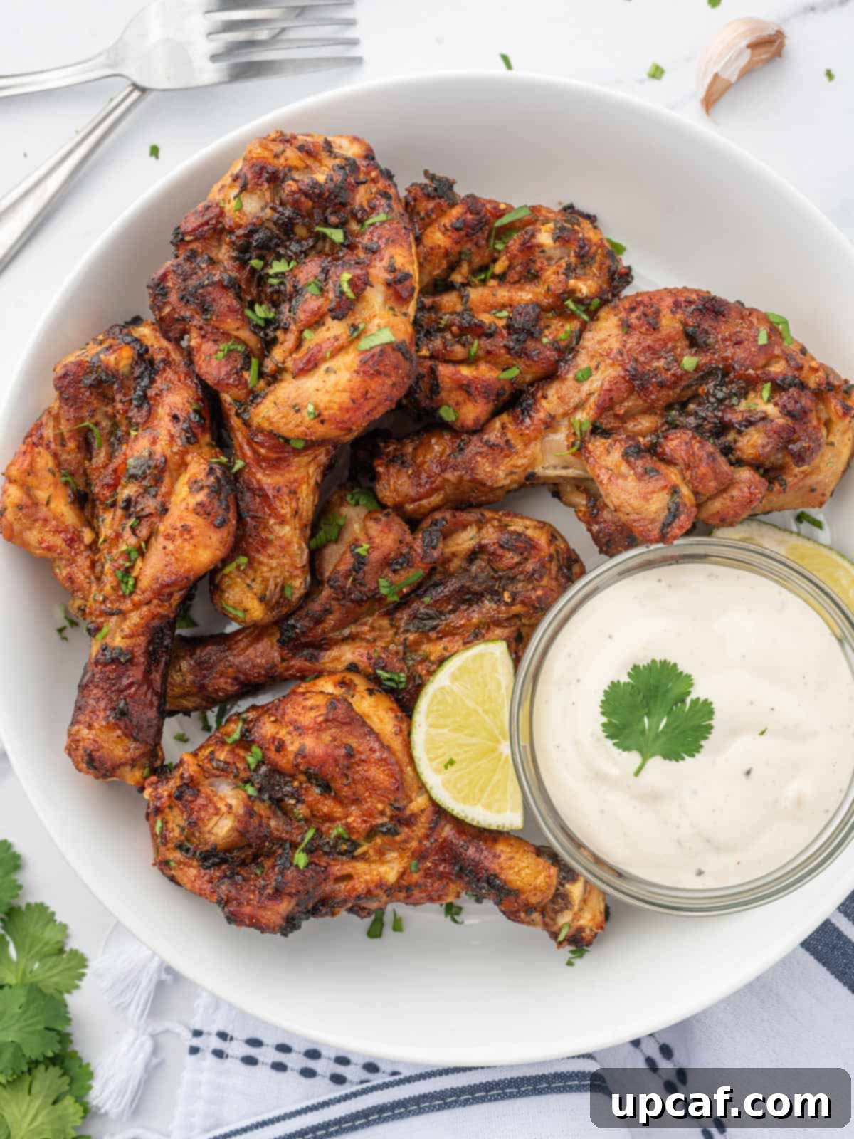 A plate of golden brown, crispy air-fried butterfly drumsticks, served with a small bowl of creamy dipping sauce and a sprinkle of fresh cilantro.