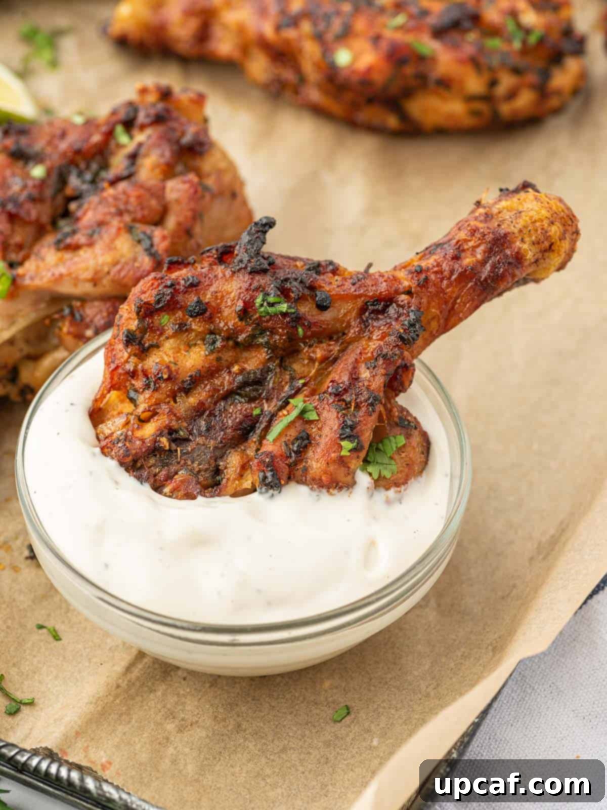 A close-up of crispy, air-fried cilantro lime chicken legs being dipped into a creamy white sauce.