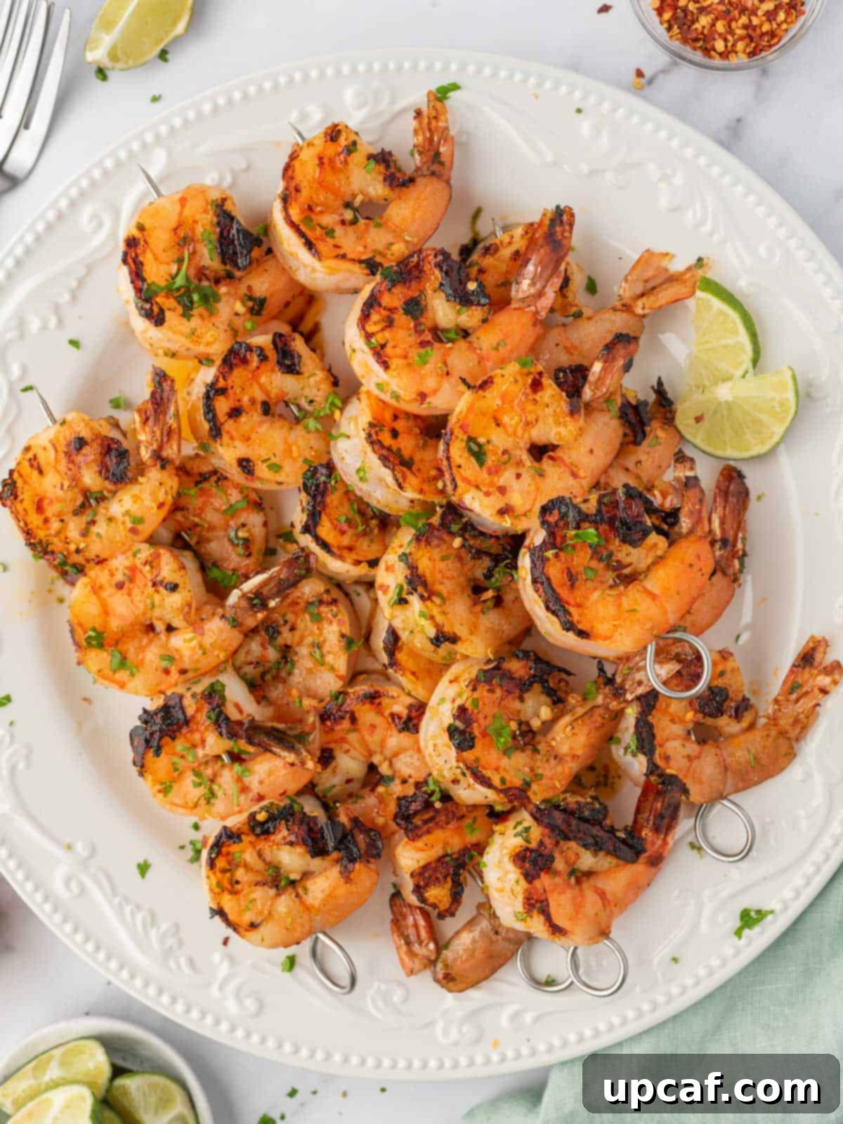 Zesty Garlic Shrimp Skewers 2 Honey lime shrimp skewers stacked on a plate with lime wedges.