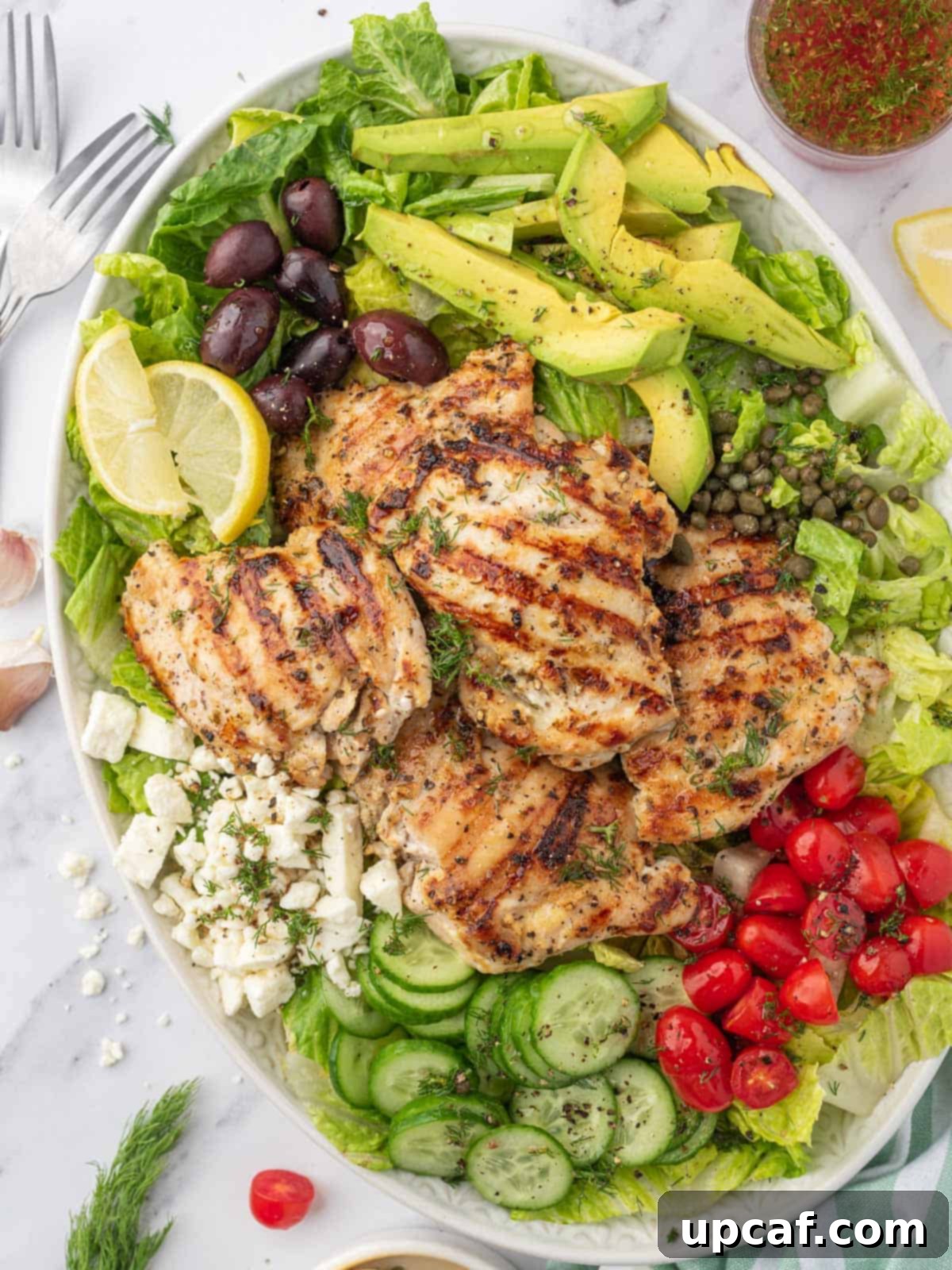 Greek chicken salad recipe on a platter with dressing on the side.