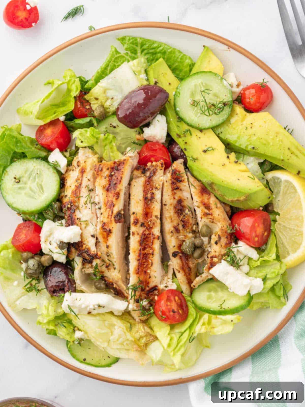 A plated portion of greek chicken salad with a fork and a napkin.