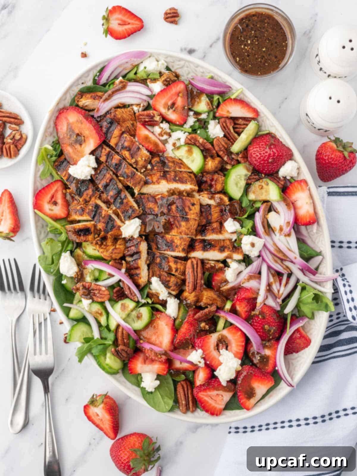 Vibrant Strawberry Grilled Chicken Salad 2 A large platter of spinach salad with strawberries and balsamic grilled chicken with several forks on the side.