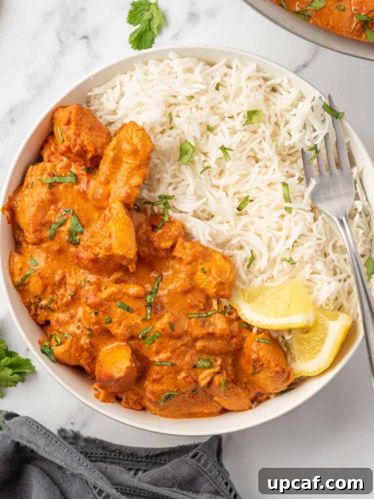 A fork rests on a bowl of healthy chicken tikka masala served with rice.