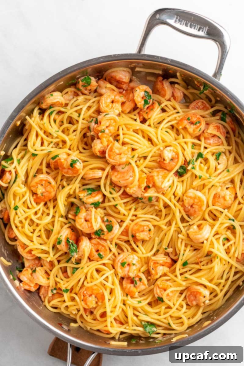 Top-down shot of a vibrant Garlic Parmesan Shrimp Spaghetti dish in a large skillet, garnished with fresh parsley.