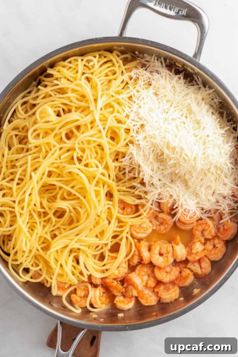 Cooked spaghetti and grated Parmesan cheese being added to the skillet with the shrimp and sauce.