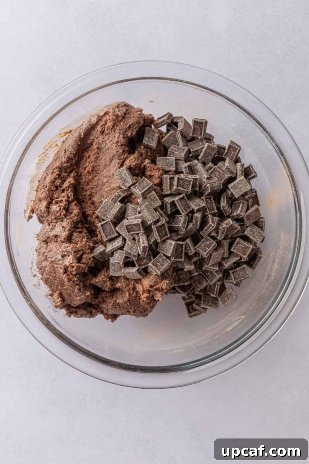 A close-up shot of vegan chocolate chunks being folded into the plant-based cookie batter, creating a rich texture.