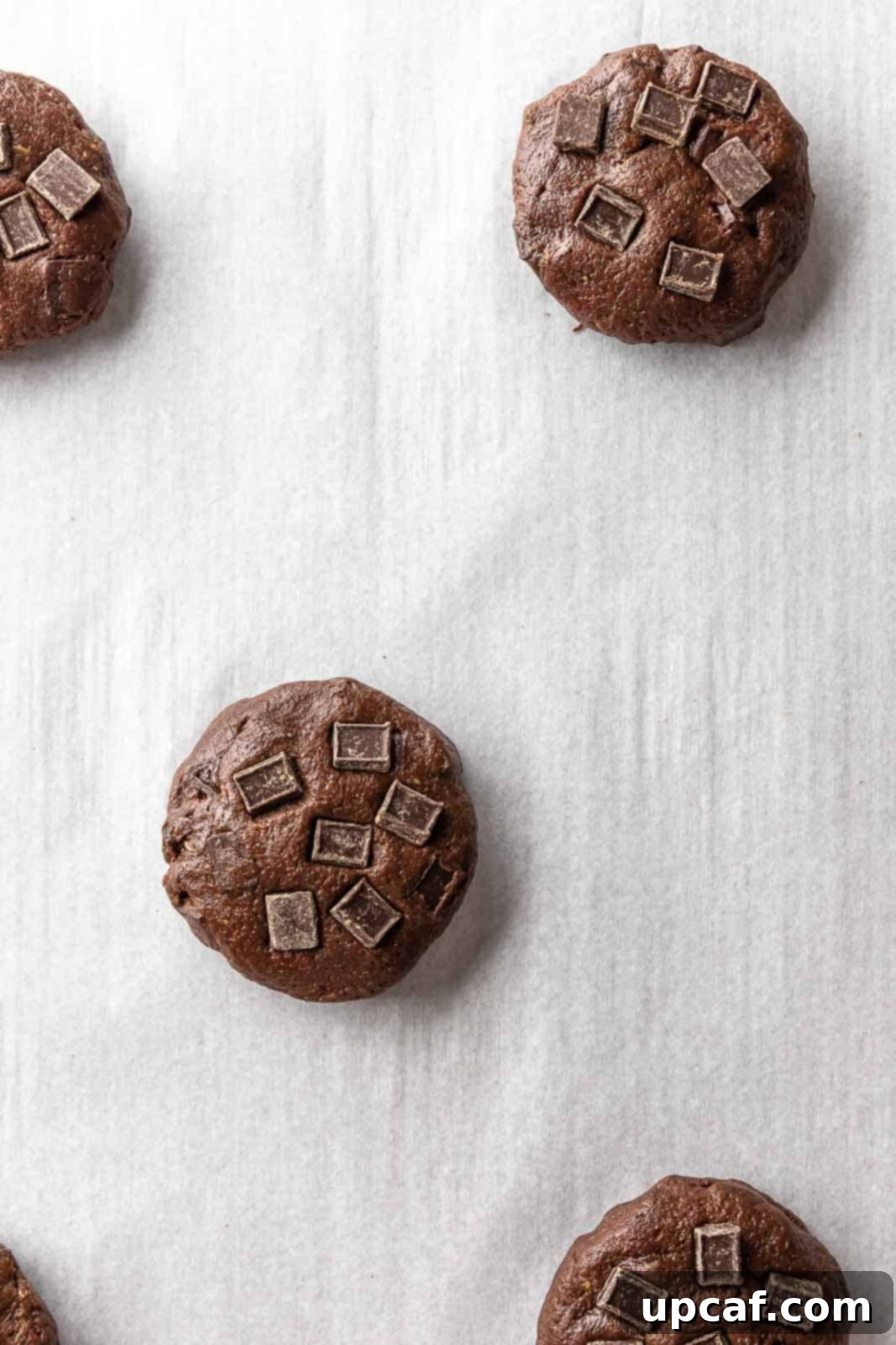 Perfectly portioned balls of unbaked vegan chocolate chip cookie dough arranged on a parchment-lined baking sheet, ready for the oven.