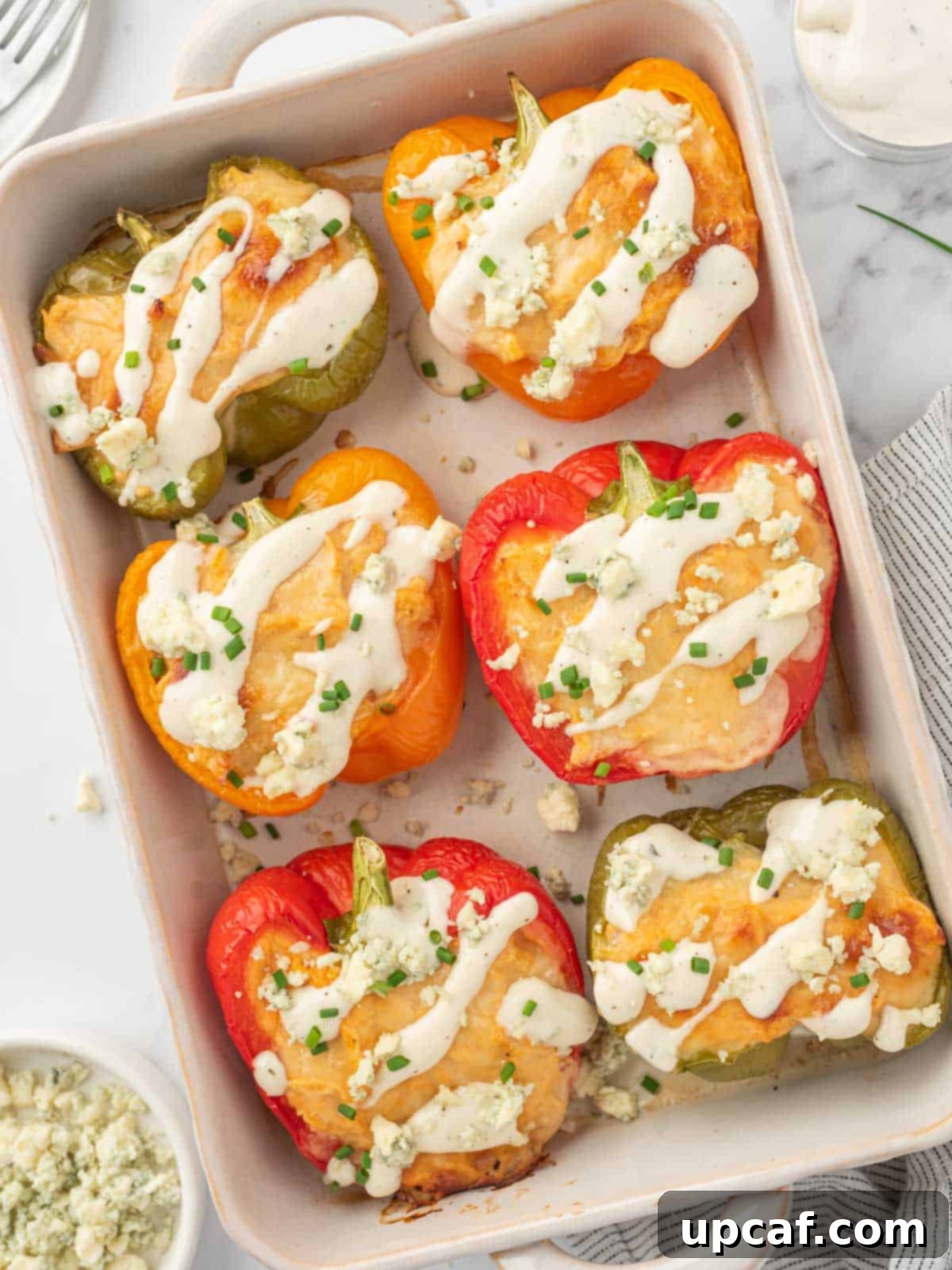 Healthy chicken stuffed peppers topped with ranch and crumbled blue cheese in a baking dish, ready to be served.