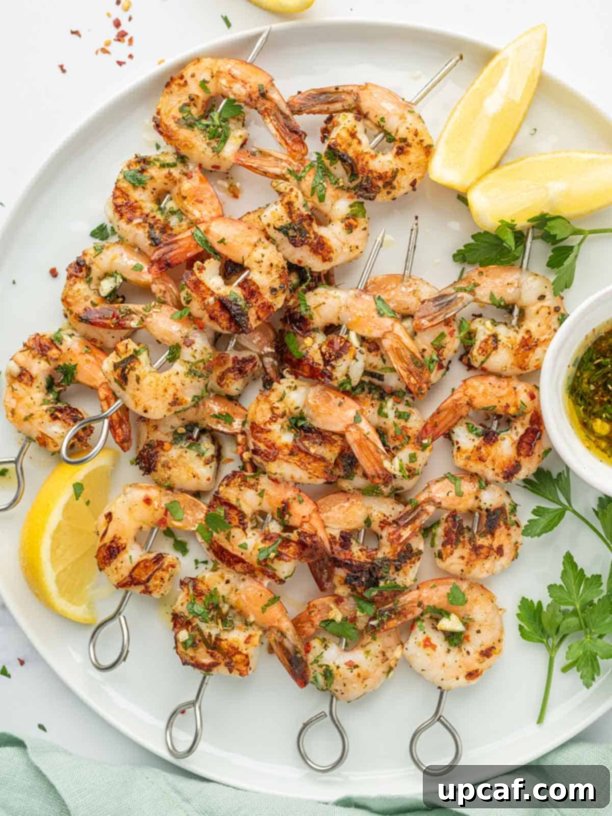 Flame-Kissed Garlic Prawns 2 Garlicky Shrimp kabobs on a platter with lemon wedges and fresh herbs.