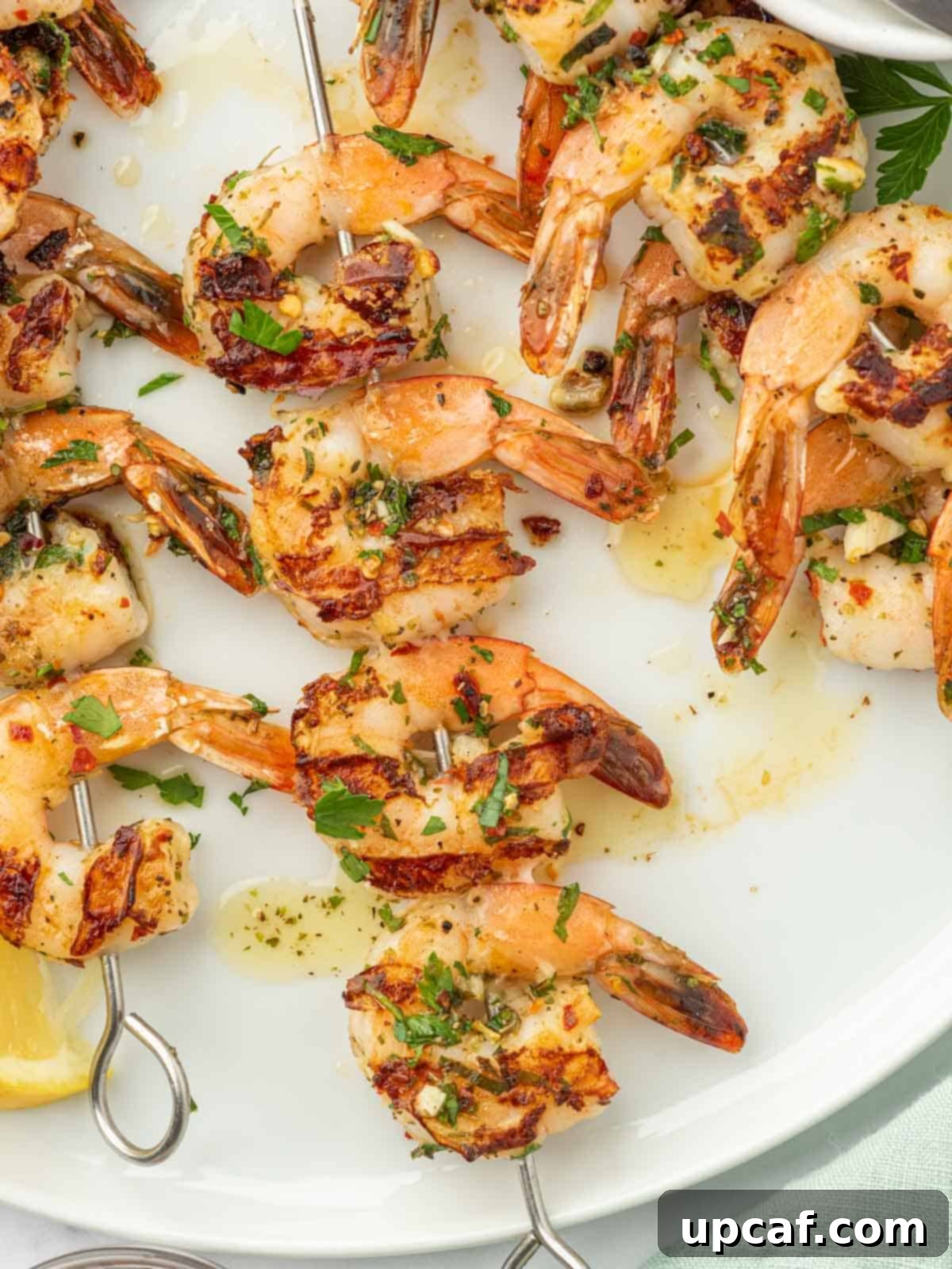 Flame-Kissed Garlic Prawns 8 Garlicky shrimp skewers on a white plate with fresh lemon and parsley.