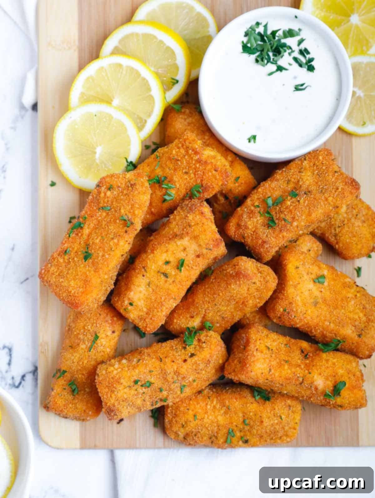 Panko baked salmon fingers on a board, served with lemon wedges and a dipping sauce.